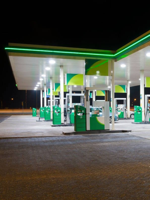 Modern fuel station forecourt at night with illuminated green fuel pumps and canopy lighting